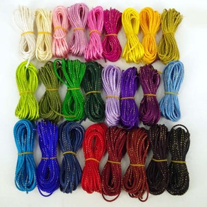 May include: A collection of 24 spools of colourful cord with gold glitter accents. The cords are arranged in rows of four, with each row featuring a different colour combination.