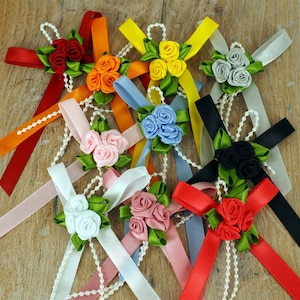May include: Assortment of ten handmade satin ribbon bows with pearl accents. Each bow features three rosettes in various colours, including red, orange, yellow, blue, pink, white, black, and green.
