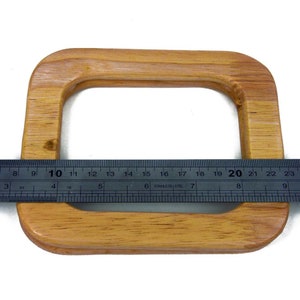 Puede incluir: Un asa de bolso rectangular de madera marr&oacute;n claro con esquinas redondeadas. Una regla met&aacute;lica se coloca sobre el asa, mostrando medidas en cent&iacute;metros. El asa mide aproximadamente 20 cm de ancho.