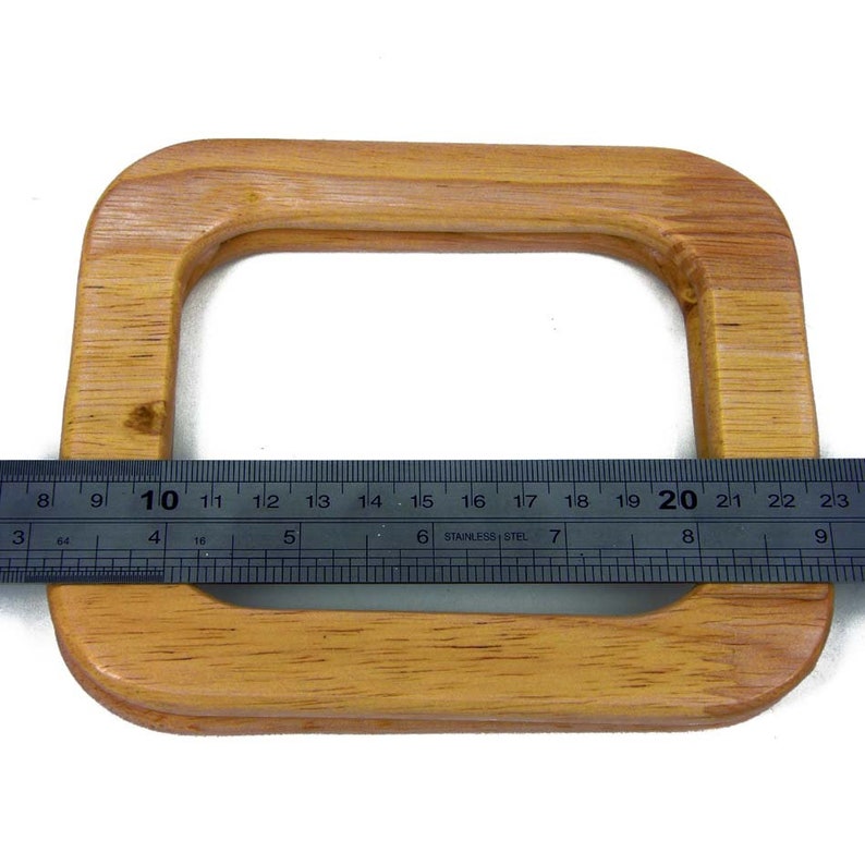 Puede incluir: Un asa de bolso rectangular de madera marr&oacute;n claro con esquinas redondeadas. Una regla met&aacute;lica se coloca sobre el asa, mostrando medidas en cent&iacute;metros. El asa mide aproximadamente 20 cm de ancho.
