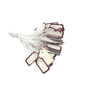 May include: A collection of rectangular price tags with a white background and a burgundy border. Each tag has a small hole at the top and is attached to a white string. The tags are blank, ready for custom text.