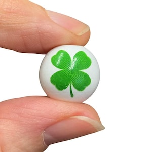 May include: A white bead with a green four-leaf clover design.