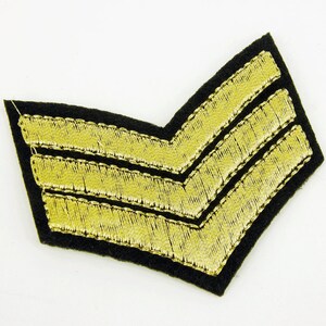 May include: A black fabric patch with two gold embroidered chevrons.