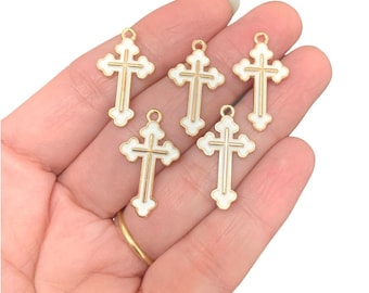 May include: Five gold-tone metal cross charms with white enamel. The crosses have a simple, traditional design.