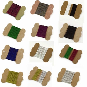 May include: Twelve spools of colourful thread wound on cardboard bobbins. The spools are arranged in four rows of three. The thread colours include red, green, blue, white, black, gold, silver, and a multi-coloured pattern.