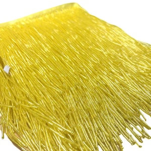 May include: A close-up of a yellow fringe trim. The fringe is made of small, thin, and shiny beads.