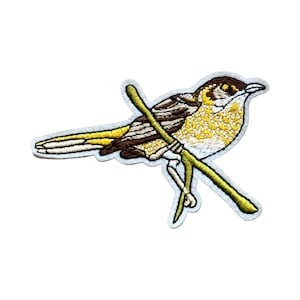 May include: Embroidered patch of a brown and yellow bird perched on a green branch. The bird has a white belly and a yellow breast.