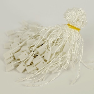 May include: A bunch of white string tags with white plastic loops. The tags are tied together with a yellow rubber band.