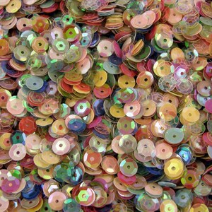May include: A large assortment of iridescent sequins in various colors, including pink, blue, green, and gold. The sequins are arranged in a random pattern and are all the same size.