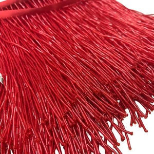 May include: Red beaded fringe trim. The fringe is made of small, cylindrical beads that are strung together to create a long, flowing fringe. The fringe is approximately 2.5 cm wide and is perfect for adding a touch of glamour to any project.