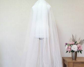 Op de afbeelding: Een witte tule bruids sluier getoond op een mannequin. De sluier is lang en vloeiend, met een zachte, delicate textuur.