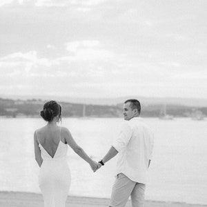 May include: A black and white photo of a couple holding hands and walking away from the camera on a beach.