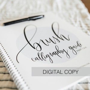 May include: A white spiral-bound brush calligraphy guide with black text that reads brush calligraphy guide part one and digital copy, accompanied by a black pen resting on the cover, featuring a light gray circular graphic element.