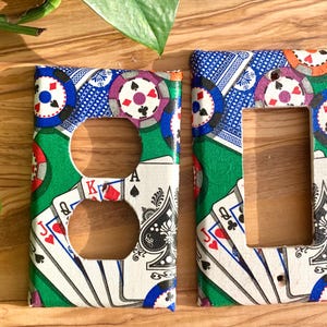 May include: Two light switch covers with a green, white, and blue playing card and poker chip design. The switch covers are made of plastic and have a glossy finish.