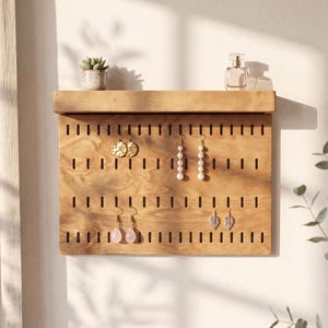 Könnte beinhalten: Ein rechteckiger Schmuckorganizer aus hellbraunem Holz mit horizontalen Schlitzen zum Aufhängen von Ohrringen. Der Organizer verfügt über eine obere Ablage mit einer kleinen Sukkulente im Topf und einem Parfümflakon aus Glas.