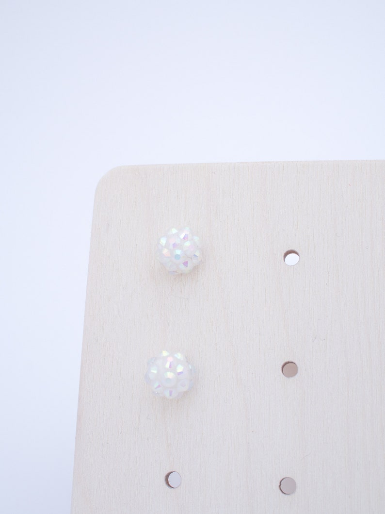 May include: A pair of iridescent white stud earrings displayed on a wooden earring holder.