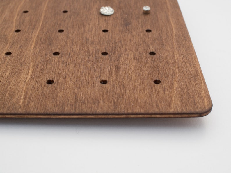 May include: A dark brown wooden board with evenly spaced holes for holding jewelry. The board has a smooth, polished finish.