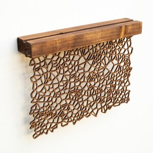 May include: A brown wooden wall hanging with a geometric design. The design is made of many small, intricate shapes that create a complex pattern. The hanging is attached to a wooden shelf.