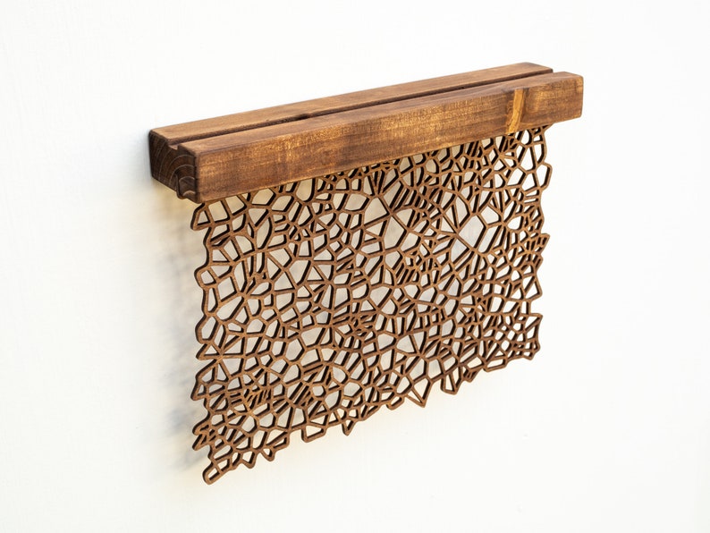 May include: A brown wooden wall hanging with a geometric design. The design is made of many small, intricate shapes that create a complex pattern. The hanging is attached to a wooden shelf.