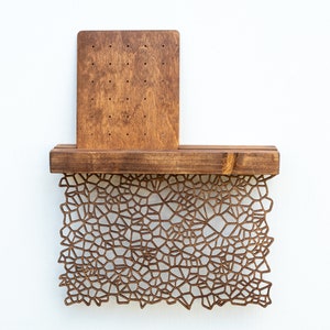 May include: A wooden wall shelf with a geometric pattern cut-out design. The shelf has a small rectangular wooden panel attached to the back.