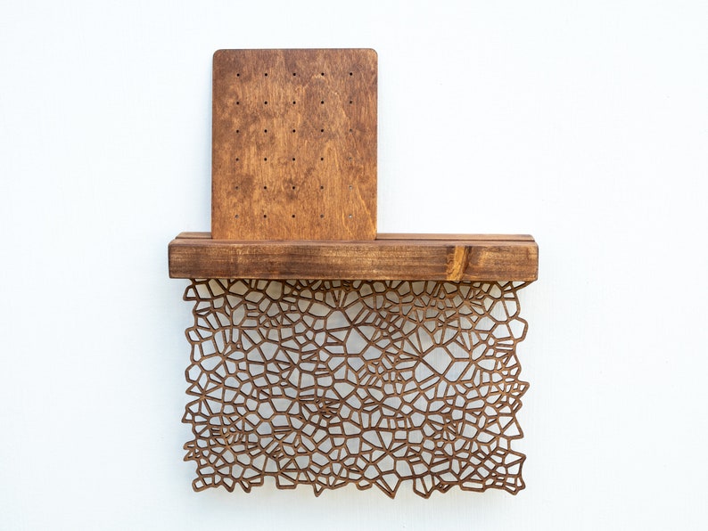 May include: A wooden wall shelf with a geometric pattern cut-out design. The shelf has a small rectangular wooden panel attached to the back.
