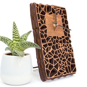 May include: A wooden clock with a geometric design, featuring a layered, intricate pattern of brown and black wood. The clock has black hands and a red second hand.
