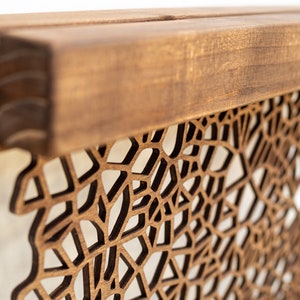 May include: A wooden wall decor with a geometric pattern cut out. The wood is a light brown color and the pattern is a dark brown color.