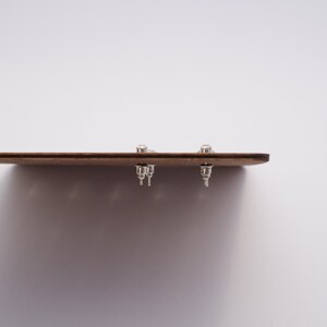 May include: A close-up of a wooden board with three silver stud earrings attached to it.