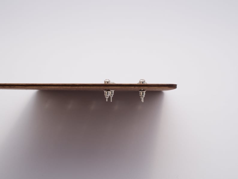 May include: A close-up of a wooden board with three silver stud earrings attached to it.