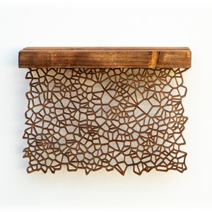 May include: A wooden shelf with a geometric pattern cut out of the front. The shelf is brown and the pattern is a light brown.