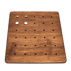 May include: A wooden earring display board with multiple holes for storing earrings. The board is dark brown and has three pairs of earrings on it.
