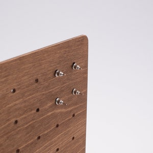 May include: A wooden earring display stand with multiple holes for storing earrings. The stand has a brown wood grain finish and is made of wood.