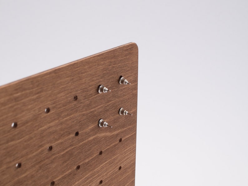 May include: A wooden earring display stand with multiple holes for storing earrings. The stand has a brown wood grain finish and is made of wood.