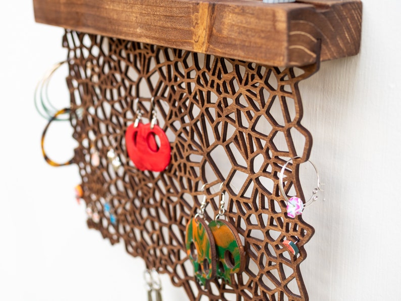 May include: Wooden earring holder with a geometric design. The holder has a shelf at the top and is decorated with various earrings in different colors and styles.