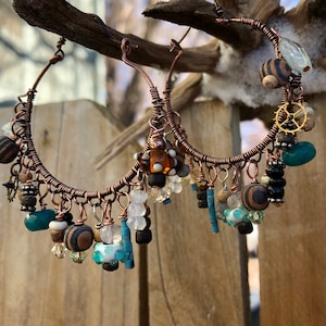 Peut inclure: Boucles d'oreilles créoles en fil de cuivre, ornées de perles marron, bleues, blanches et transparentes. Les boucles présentent des perles en bois, de petits engrenages et d'autres éléments décoratifs, pour un look artisanal unique.