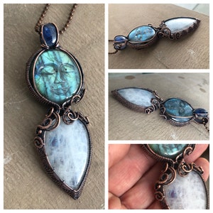 Op de afbeelding: Handgemaakte koperdraad hangerketting met een grote, gebeeldhouwde labradorietsteen met een gezichtsontwerp, een druppelvormige maansteen en een blauwe steen accent. De hanger hangt aan een koperen ketting.