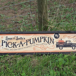 May include: A wooden sign with black lettering and a black frame. The sign reads "Linus & Sally's PICK-A-PUMPKIN & COME SEE THE GREAT PUMPKIN ON HALLOWEEN $1". The sign also features a cartoon image of a black pickup truck with a pumpkin in the bed.