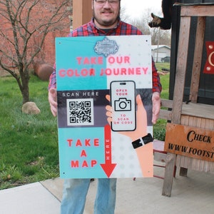 May include: A blue and red sign with the text "Take Our Color Journey" and a QR code. The sign also has a red arrow pointing down with the text "Take A Map Here".