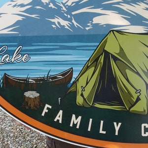 May include: A colorful oval sign with a mountain scene, a lake, a canoe, a green tent, and the text "Lake Family Camping".