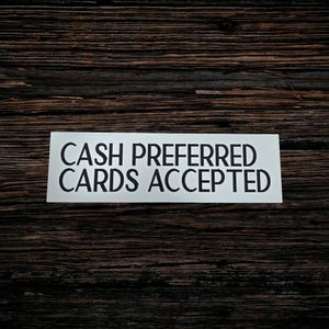 May include: A rectangular white sign with black text that reads CASH PREFERRED CARDS ACCEPTED. The sign features a clean, sans-serif font and is presented as a clear, legible notice for customers regarding payment methods at a point of sale.