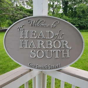May include: A brown oval sign with white lettering that reads "Welcome to The Head of the Harbor, South. One Smith Street."