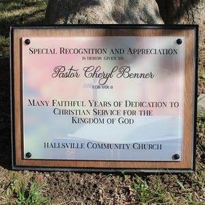 May include: A framed plaque with the text "Special Recognition and Appreciation" given to "Pastor Cheryl Benner" for years of dedication to Christian service. The plaque is from Hallsville Community Church.
