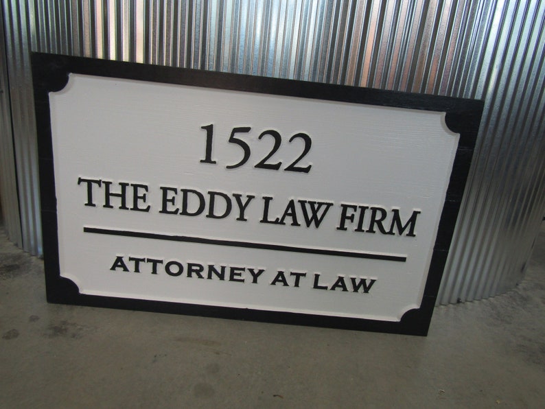 Puede incluir: Un letrero rectangular blanco con borde y letras negras. El letrero dice "1522 The Eddy Law Firm Attorney at Law".