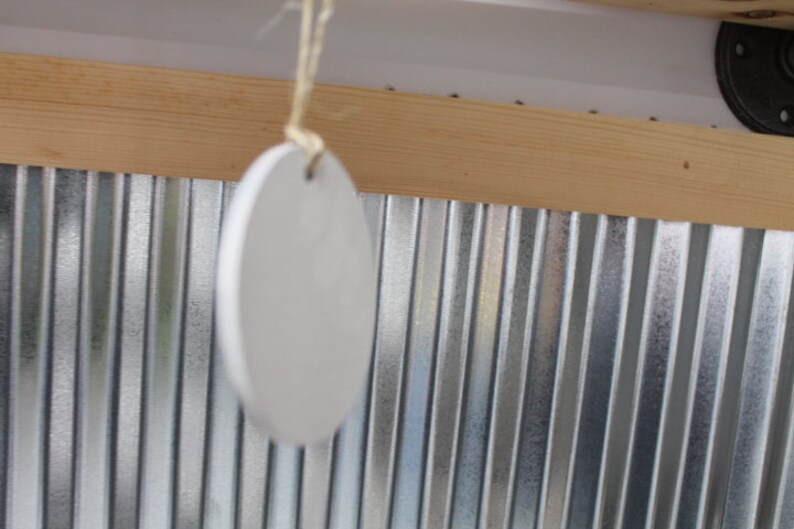 May include: A white ceramic ornament hangs from a string against a backdrop of corrugated metal and wood.
