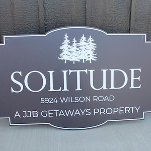 May include: A brown wooden sign with white text that reads "SOLITUDE", "5924 WILSON ROAD", and "A JJB GETAWAYS PROPERTY". The sign has a stylized image of five trees in the upper left corner.