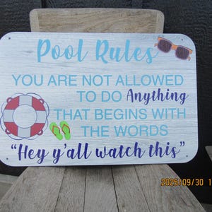 May include: A rectangular wooden sign with the words "Pool Rules" in light blue script. The sign includes the text "YOU ARE NOT ALLOWED TO DO Anything THAT BEGINS WITH THE WORDS 'Hey y'all watch this'" with illustrations of sunglasses, a life preserver, and flip-flops.