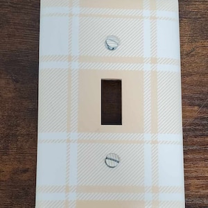 May include: A light beige and white plaid light switch cover with two silver screws.