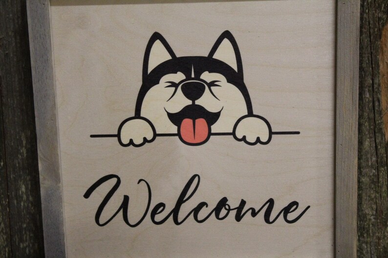 May include: A wooden sign with a black and white cartoon dog peeking over the top. The dog has a pink tongue sticking out and the sign says "Welcome".