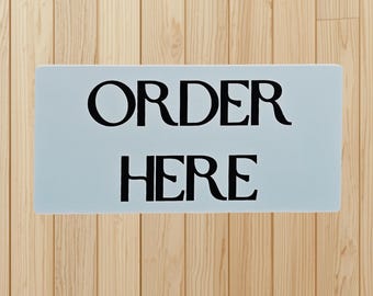 Order Here Sign – Bold Black Lettering on Light Background for Café, Restaurant, Food Truck, or Small‑Business Counter Decor