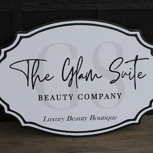 May include: White oval sign with black trim and the text "The Glam Suite Beauty Company Luxury Beauty Boutique" in black script font.